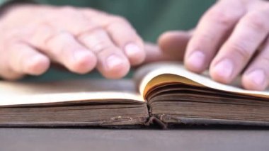 Evde ya da kütüphanede kitap okuyan bir adamın eli. Eski bir kitabın sayfalarını çevirip kapat.