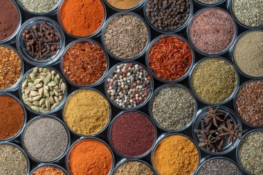 Arka planda yemek pişirmek için aromatik baharatlar, tohumlar ve kuru otlar küçük cam kaselerde, yakın plan, üst görüş