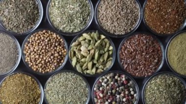 Arka planda yemek pişirmek için çeşitli aromatik baharatlar, tohumlar ve kuru otlar. Smal cam kaselerde dönüyorlar, kapatıyorlar, üstten bakıyorlar.