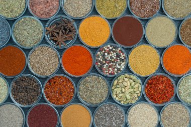Arka planda yemek pişirmek için aromatik baharatlar, tohumlar ve kuru otlar küçük cam kaselerde, yakın plan, üst görüş