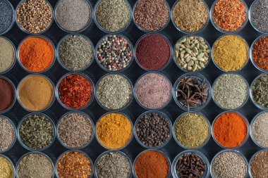 Arka planda yemek pişirmek için aromatik baharatlar, tohumlar ve kuru otlar küçük cam kaselerde, yakın plan, üst görüş