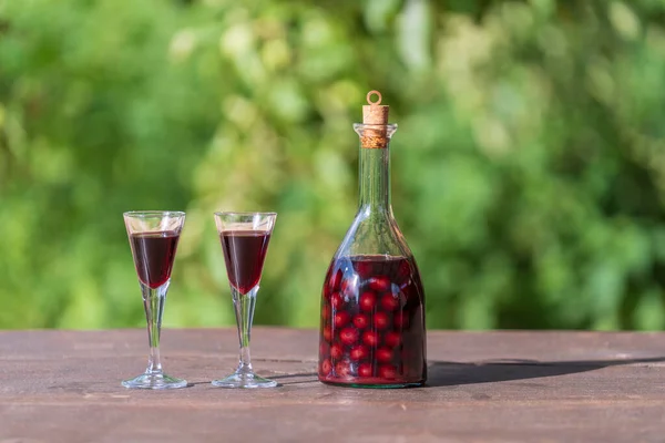 夏の庭の木のテーブルの上に2つのガラスとガラスボトルの自家製チェリーブランデー クローズアップ — ストック写真