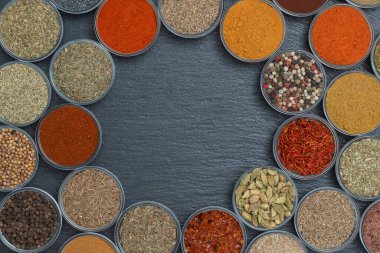 Arka planda yemek pişirmek için aromatik baharatlar, tohumlar ve kuru otlar küçük cam kaselerde, yakın plan, üst manzara. Metin için kopyalama alanı olan siyah sayfadaki baharat çeşitliliği