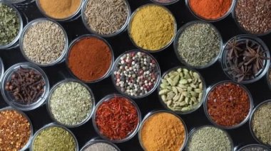 Arka planda yemek pişirmek için çeşitli aromatik baharatlar, tohumlar ve kuru otlar. Smal cam kaselerde dönüyorlar, kapatıyorlar, üstten bakıyorlar.