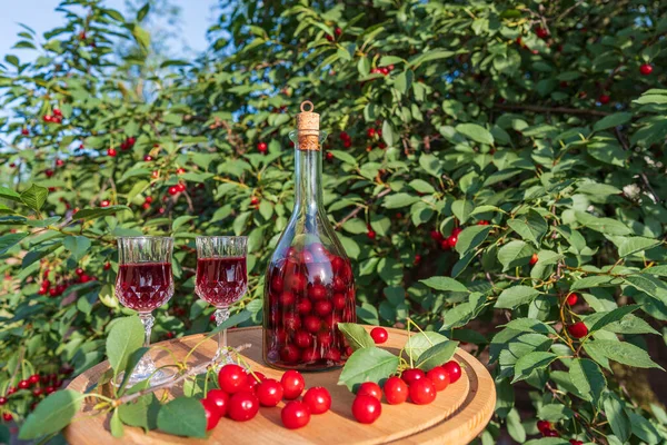 在夏日花园的一张木制桌子上 一个自制的樱桃白兰地酒杯和一个玻璃瓶 关门了 — 图库照片