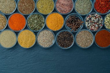 Arka planda yemek pişirmek için aromatik baharatlar, tohumlar ve kuru otlar küçük cam kaselerde, üst görünümü kapat, boşluğu kopyala