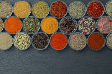 Arka planda yemek pişirmek için aromatik baharatlar, tohumlar ve kuru otlar küçük cam kaselerde, üst görünümü kapat, boşluğu kopyala