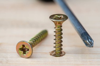 Golden screws screwed into wooden plank and screwdriver, close up