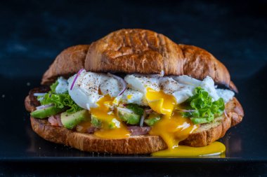 Kavrulmuş yumurta, somon ve avokado ile kaplanmış siyah arka planda kruvasan taze sandviç.