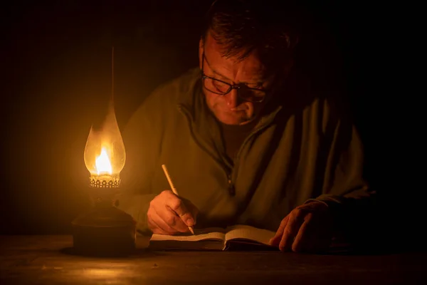 Man writes with a pencil in a notebook by the light of a kerosene lamp , night time, close up