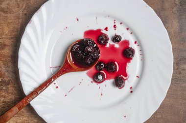 Beyaz tabakta kırmızı kiraz reçeli, tahta kaşıkla, yaklaş, üst manzara