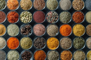 Arka planda yemek pişirmek için aromatik baharatlar, tohumlar ve kuru otlar küçük cam kaselerde, yakın plan, üst görüş