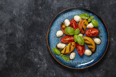 Grilled peach salad with mozzarella, tomato, green basil and sauce. Fresh gourmet salad in plate on black background, close up, top view, copy space