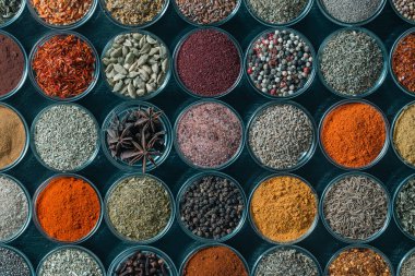 Arka planda yemek pişirmek için aromatik baharatlar, tohumlar ve kuru otlar küçük cam kaselerde, yakın plan, üst görüş