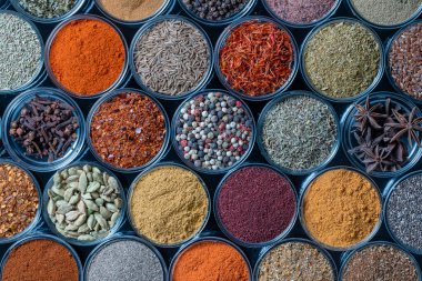 Arka planda yemek pişirmek için aromatik baharatlar, tohumlar ve kuru otlar küçük cam kaselerde, yakın plan, üst görüş