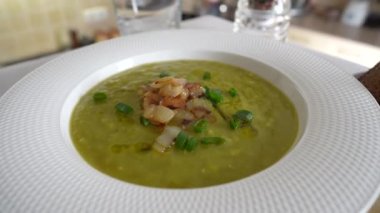 Beyaz tabakta yeşil bezelye kremalı çorba, masada baharatlar, döndür, kapat. Sağlıklı yemek, lezzetli kurutulmuş yeşil bezelye çorbası.