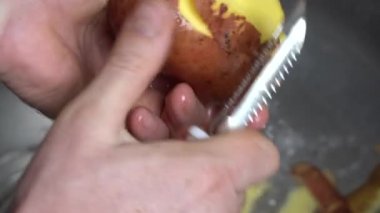 Male hands peeling potatoes with a knife in the kitchen above the kitchen sink with sound, close up. Fresh, washed potato and man hands with knife