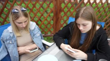 Relaxed two young girls using smartphone surfing social media, checking news, playing mobile games or texting messages sitting in street cafe, close up