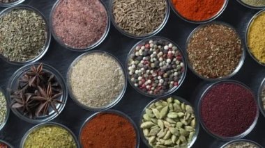 Arka planda yemek pişirmek için çeşitli aromatik baharatlar, tohumlar ve kuru otlar. Smal cam kaselerde dönüyorlar, kapatıyorlar, üstten bakıyorlar.