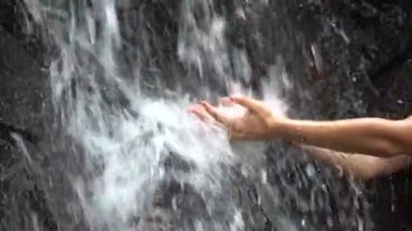 Woman hands under the water of a waterfall in the mountains. Cupped female hands gathering fresh clean source water, close up, slow motion