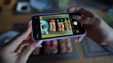 Kız, rahat Japon restoranında akıllı telefon kullanarak suşi fotoğrafı çekiyor. Kadın eli, modern akıllı telefonla yiyeceklerin fotoğrafını çeker. Yaklaş, 4K