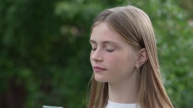 Doğada bir bardaktan maden suyu içen ve kameraya bakarken gülümseyen genç bir kızın portresi, kapat. Yaşam tarzı sağlık hizmeti kavramı