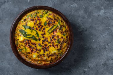 Ceramic bowl with vegetable frittata, simple vegetarian food. Frittata with eggs, green beet leaves, onion, pepper, spices and cheese, close up. Italian egg omelette, top view, copy space