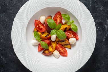 Peynirli ızgara şeftali salatası, domates, yeşil fesleğen ve sos. Siyah arka planda beyaz tabakta taze gurme salatası, yakın plan, üst görünüm