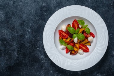 Peynirli ızgara şeftali salatası, domates, yeşil fesleğen ve sos. Siyah arkaplanda beyaz tabakta taze gurme salatası, yakın plan, üst görünüm, boşluk kopyala