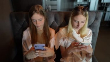 İki genç kız akıllı telefon kullanarak sosyal medyada geziniyor, haberleri kontrol ediyor, mobil oyunlar oynuyor ya da kanepede oturmuş mesaj yazıyor, kapatıyorlar.