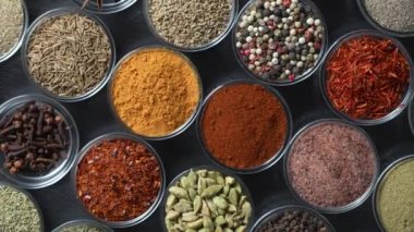 Arka planda yemek pişirmek için çeşitli aromatik baharatlar, tohumlar ve kuru otlar. Smal cam kaselerde dönüyorlar, kapatıyorlar, üstten bakıyorlar.