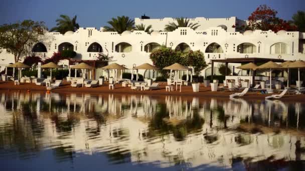 サンラウンジャー パラソルは エジプトの日の出の間にシャルム シェイクのリゾートタウンのビーチの穏やかな海の水に反映されています — ストック動画