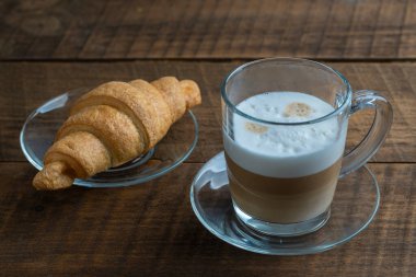 Sabah kahvaltısı için ahşap masada ayçöreği olan bir bardak taze kapuçino kahvesi.
