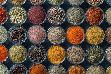 Arka planda yemek pişirmek için aromatik baharatlar, tohumlar ve kuru otlar küçük cam kaselerde, yakın plan, üst görüş