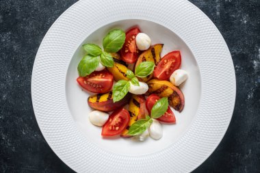 Peynirli ızgara şeftali salatası, domates, yeşil fesleğen ve sos. Siyah arka planda beyaz tabakta taze gurme salatası, yakın plan, üst görünüm