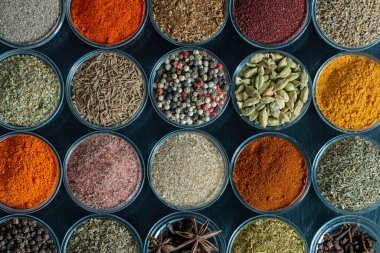 Arka planda yemek pişirmek için aromatik baharatlar, tohumlar ve kuru otlar küçük cam kaselerde, yakın plan, üst görüş