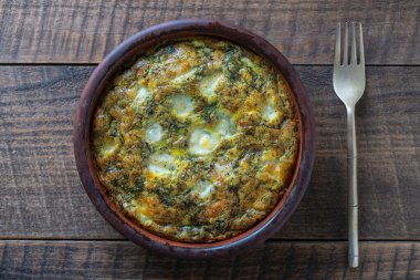 Sebzeli frittata ile seramik kase, basit vejetaryen yemeği. Yumurtalı frittata, yeşil pancar yaprakları, soğan, biber, baharat ve peynir, ahşap masada, yakın çekim. İtalyan omleti, üst manzara.