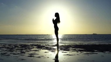 Gün batımında tropikal plajda yoga yapan kadın silueti. Beyaz kız deniz suyunun yanında yoga yapıyor.