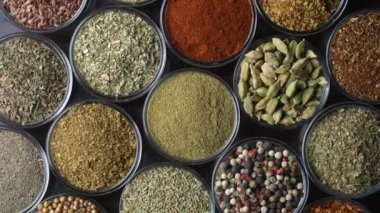 Arka planda yemek pişirmek için çeşitli aromatik baharatlar, tohumlar ve kuru otlar. Smal cam kaselerde dönüyorlar, kapatıyorlar, üstten bakıyorlar.