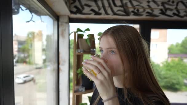 Μια Σκεπτική Νεαρή Κοπέλα Κοιτάζει Έξω Από Παράθυρο Και Πίνει — Αρχείο Βίντεο