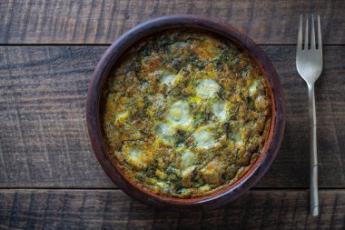 Sebzeli frittata ile seramik kase, basit vejetaryen yemeği. Yumurtalı frittata, yeşil pancar yaprakları, soğan, biber, baharat ve peynir, ahşap masada, yakın çekim. İtalyan omleti, üst manzara.