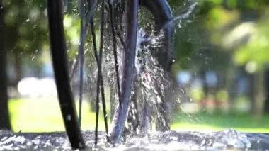 Güneşli bir günde Batumi şehrinde su sıçrayan güneş ışığına karşı güzel bir çeşme ve bisiklet tekerleği, Georgia. Ağır çekim, yakın çekim.