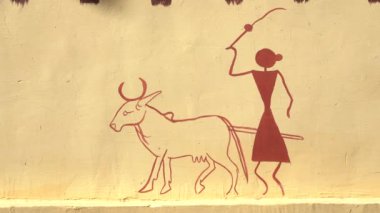 UDAIPUR, INDIA - NOVEMBER 22, 2018: Udaipur, Rajasthan, Hindistan 'da sarı çit duvarındaki dekoratif geleneksel çizimler, çekim tespiti. İnek otlatan kadın figürü.