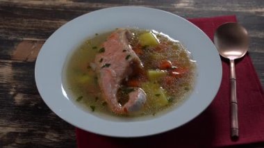 Fresh salmon fish soup with carrots, potatoes and herbs in a white plate, close up, rotates.Tasty dinner consists of a fish soup with salmon