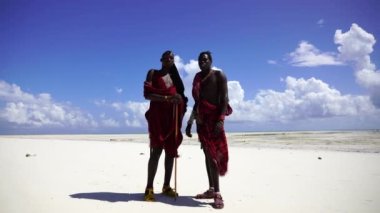 Zanzibar, Tanzanya - 12 Aralık 2019: Geleneksel kıyafetler giymiş iki Afrikalı adam okyanus kenarında, Tanzanya, Doğu Afrika 'daki Zanzibar adasının kumsalında duruyor.