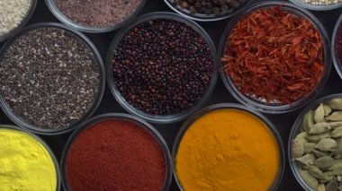 Arka planda farklı baharatlar ve bitkiler dönüyor, yakın plan, üst görünüm. Renkli baharatlar, tohumlar ve yemek pişirmek için bitkiler.