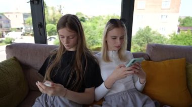 İki genç kız akıllı telefon kullanarak sosyal medyada geziniyor, haberleri kontrol ediyor, mobil oyunlar oynuyor ya da kanepede oturmuş mesaj yazıyor, kapatıyorlar.