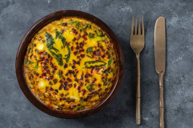 Ceramic bowl with vegetable frittata, simple vegetarian food. Frittata with eggs, green beet leaves, onion, pepper, spices and cheese, close up. Italian egg omelette, top view
