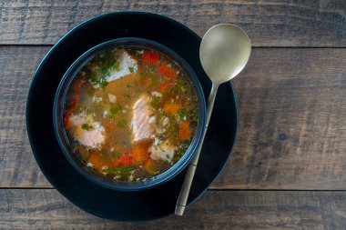 Tahta masadaki siyah tabakta havuçlu, patatesli ve kırmızı biberli taze somon balığı çorbası. Lezzetli akşam yemeği somonlu balık çorbasından oluşur. Üst görünüm