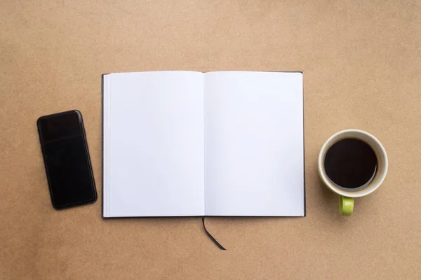 Top view with blank notebook,cup of coffee and smartphone on brown wood table background.